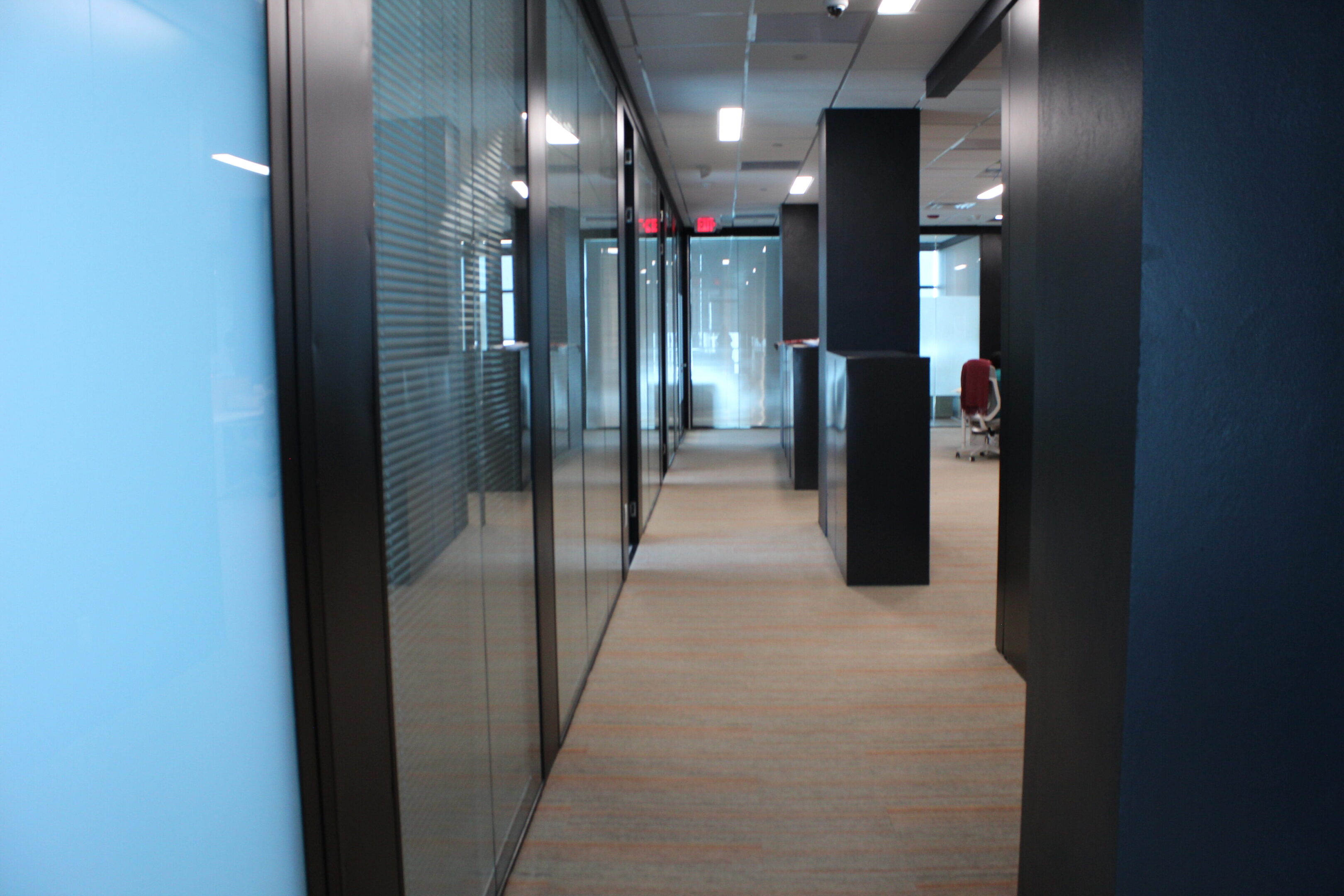 Modern office hallway with glass walls and carpeted floors.