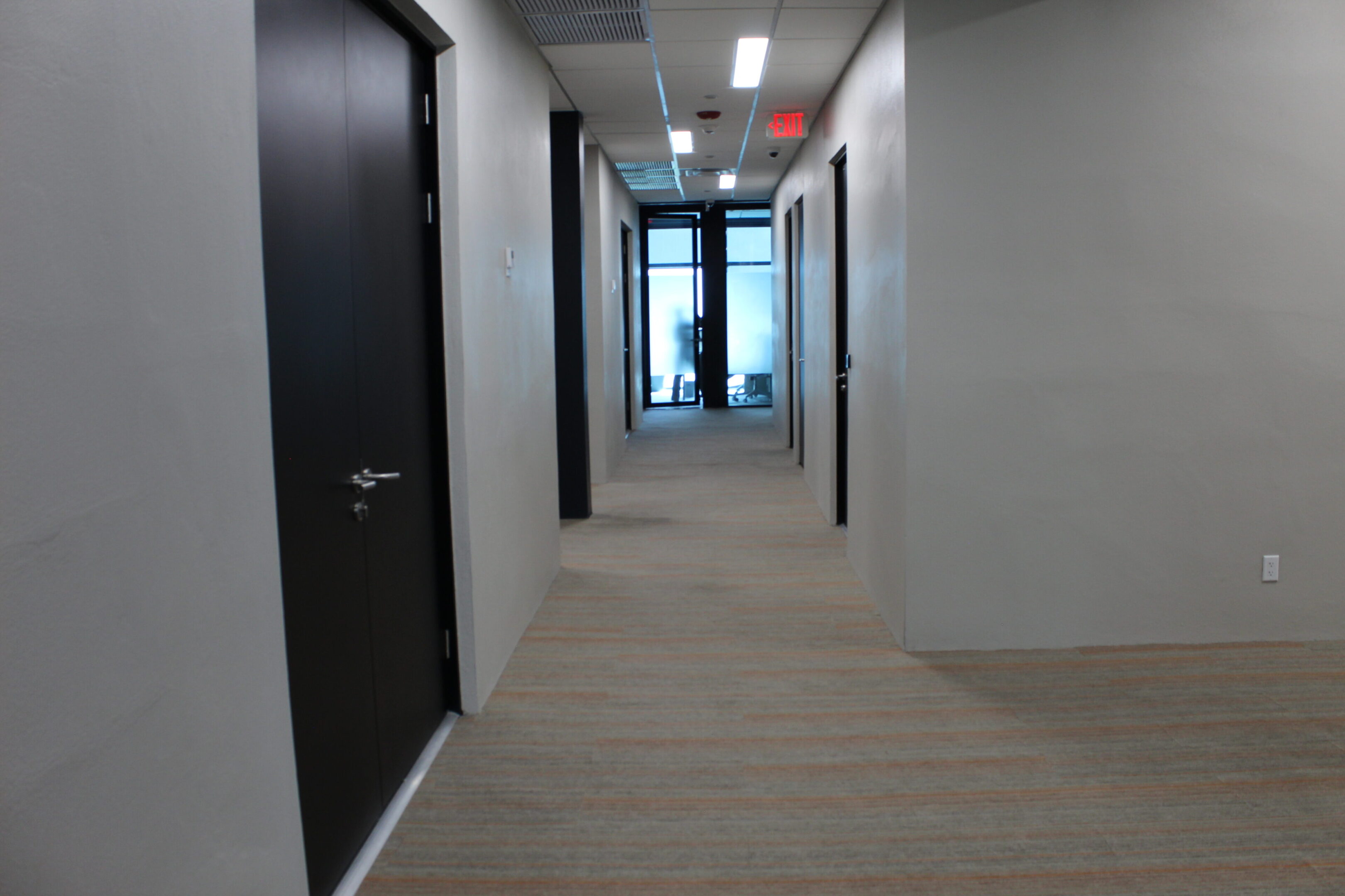 A clean, modern hallway with closed black doors and a glass exit at the end.