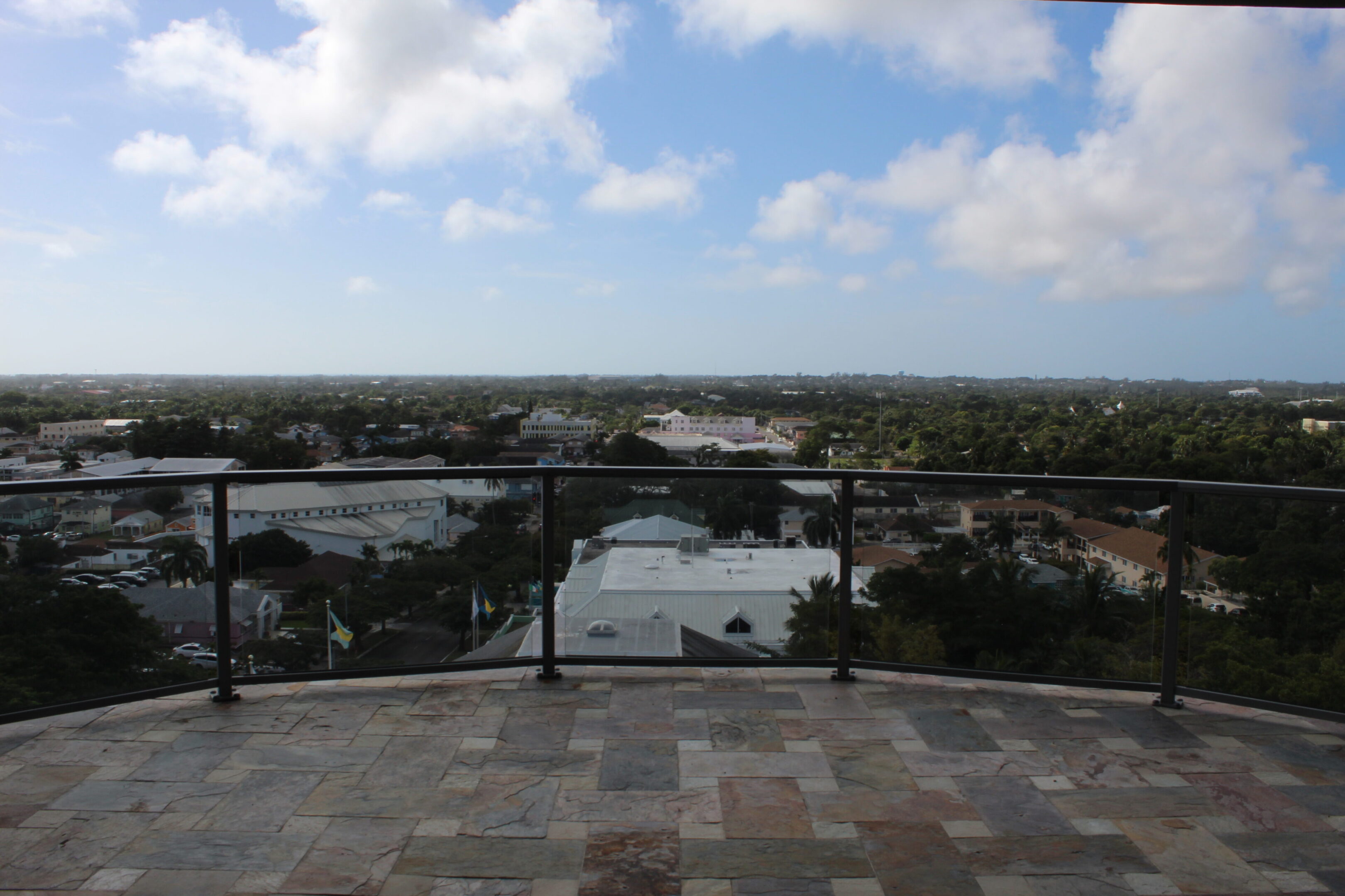 Scenic waterfront view from a terrace with a glass railing under a partly cloudy sky.