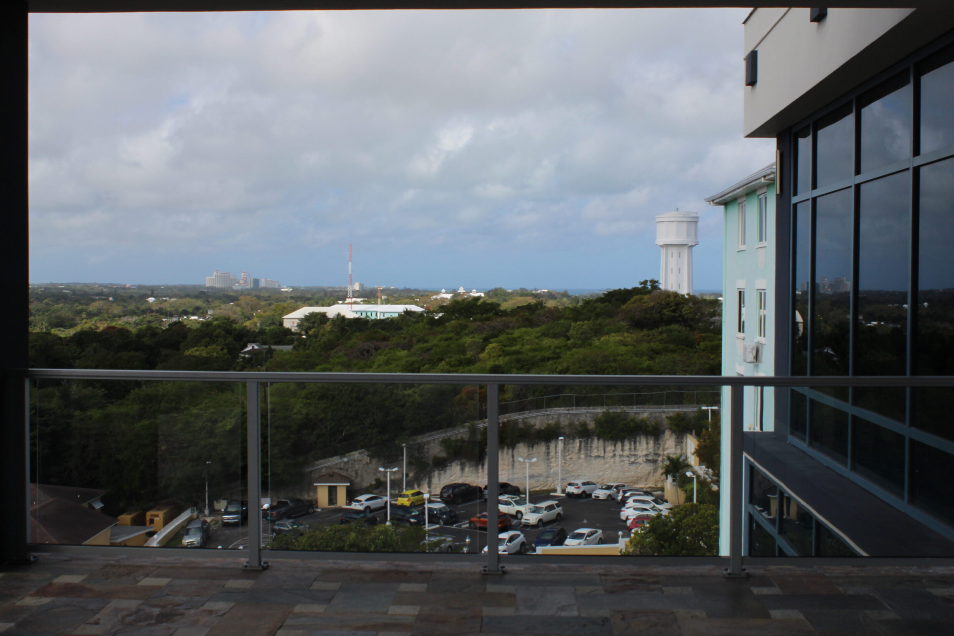 View of a parking lot and greenery from a balcony with a cloudy sky.