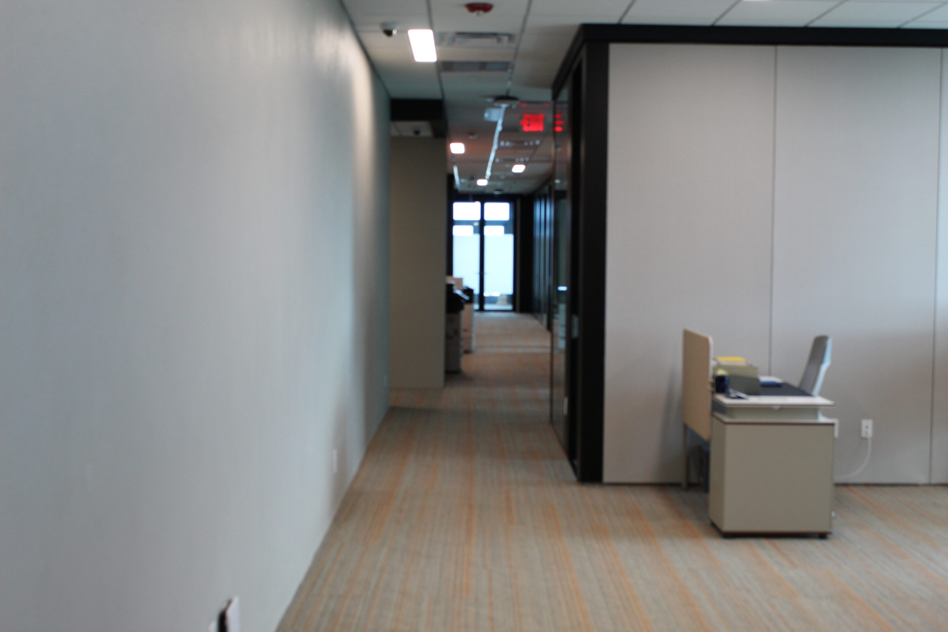 A view down an office hallway with cubicles and a glass door at the end.