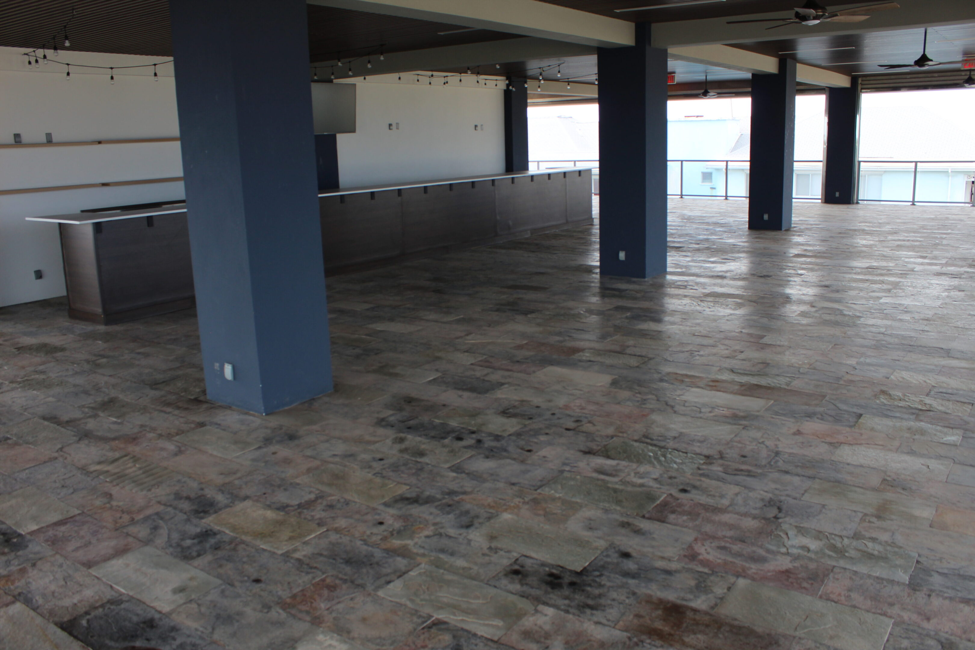 Empty covered patio with tiled floor and blue pillars.