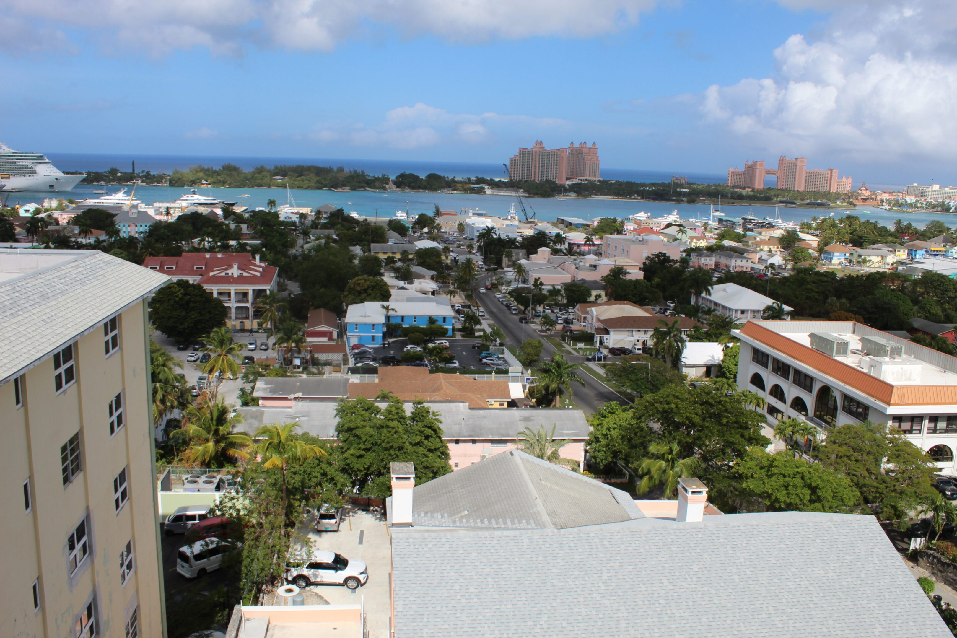 View of a coastal town with rooftops and ocean in the distance under a partly cloudy sky.