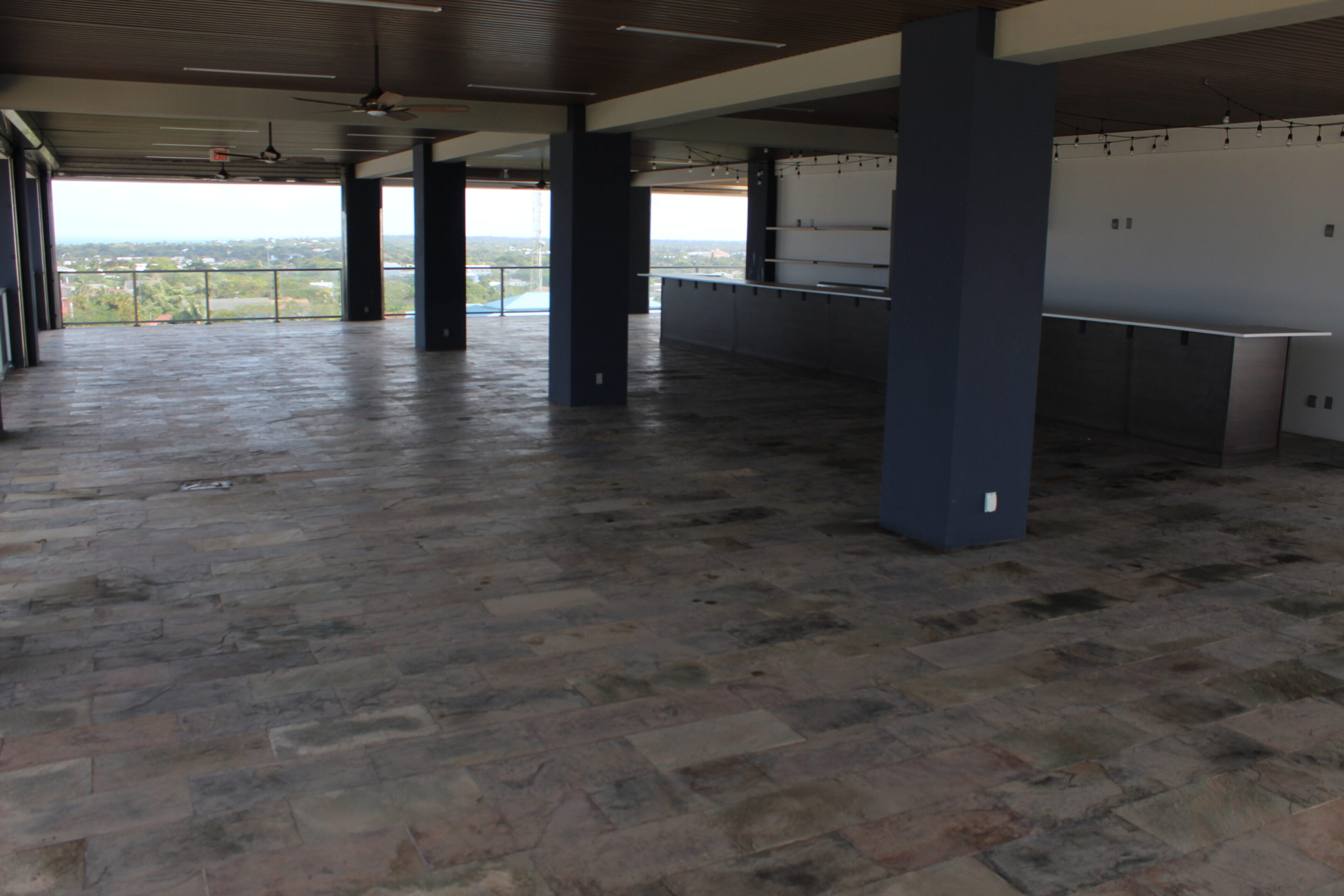 Empty covered terrace with tiled floor and supporting pillars.