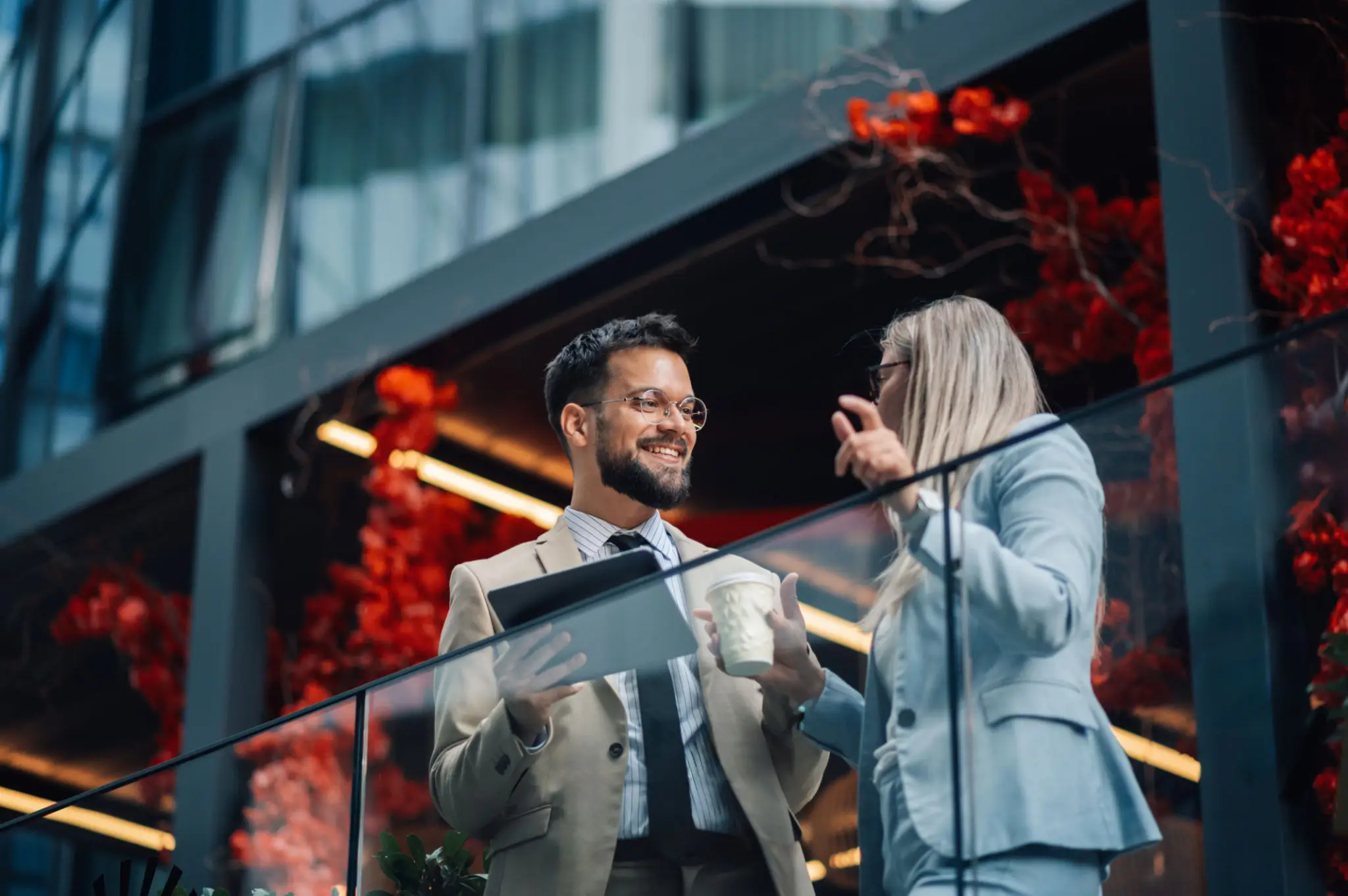 Two professionals discuss work on a balcony with a city backdrop.